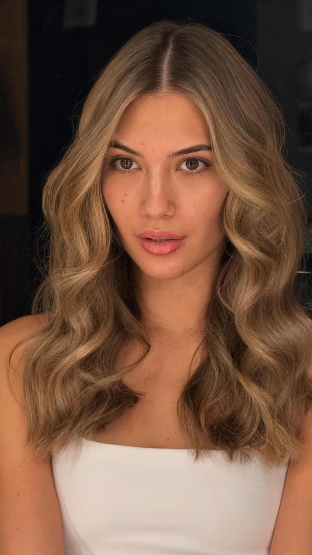 Woman with wavy blonde hair wearing a white top against a dark background